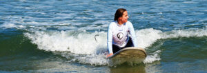 surfer girl rides a wave on the surf lesson under the sunshine, with a big smile. In Praia Azul - Santa Cruz, Portugal