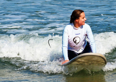 surfer girl rides a wave on the surf lesson under the sunshine, with a big smile. In Praia Azul - Santa Cruz, Portugal
