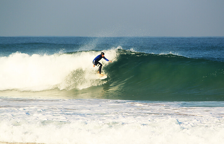 Surfer on a green wave in Praia Azul - Santa Cruz, Portugal during surf lesson. Sunshine day and clear water