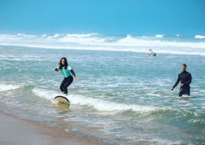 Surfer girls just want to have fun. Small group of beginner surfers on the safety of an Atlantic Coast Surf School surf lesson with the close presence of professional surf teacher